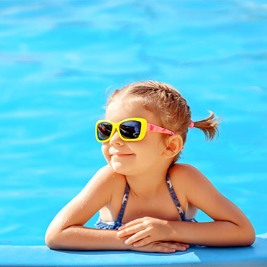 Una niña pequeña sonríe en el borde de una piscina. La dureza del agua de las piscinas puede dañar sus superficies y corroer las tuberías.